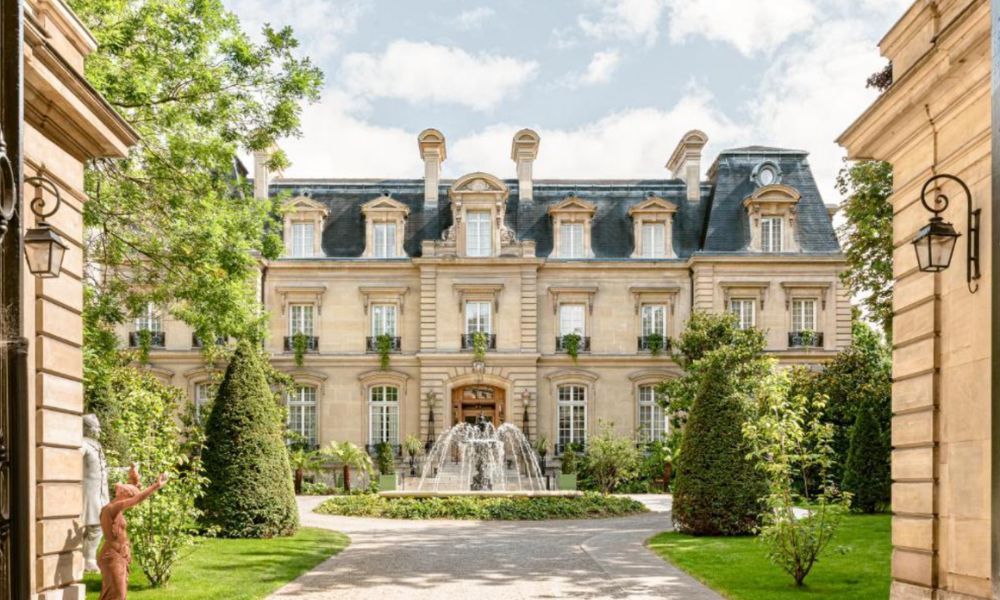 This is an image of a massive chateau with a fountain and lots of greenery.