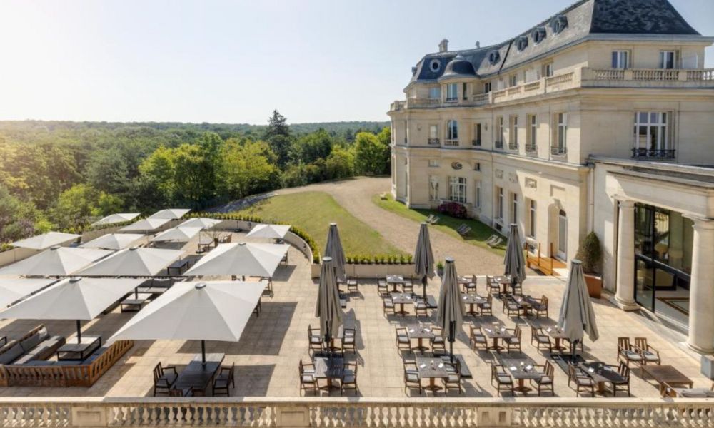This is an image of a castle with a big outdoor area full of tables and chairs and umbrellas.