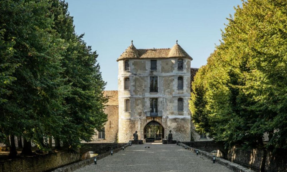 This is an chateau that has old stone walls, and trees lining the path up to its entrance.