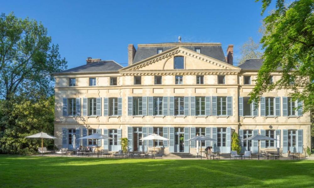 This is an image of a chateau that is large and has plenty of windows and a lush green field of grass out the front.