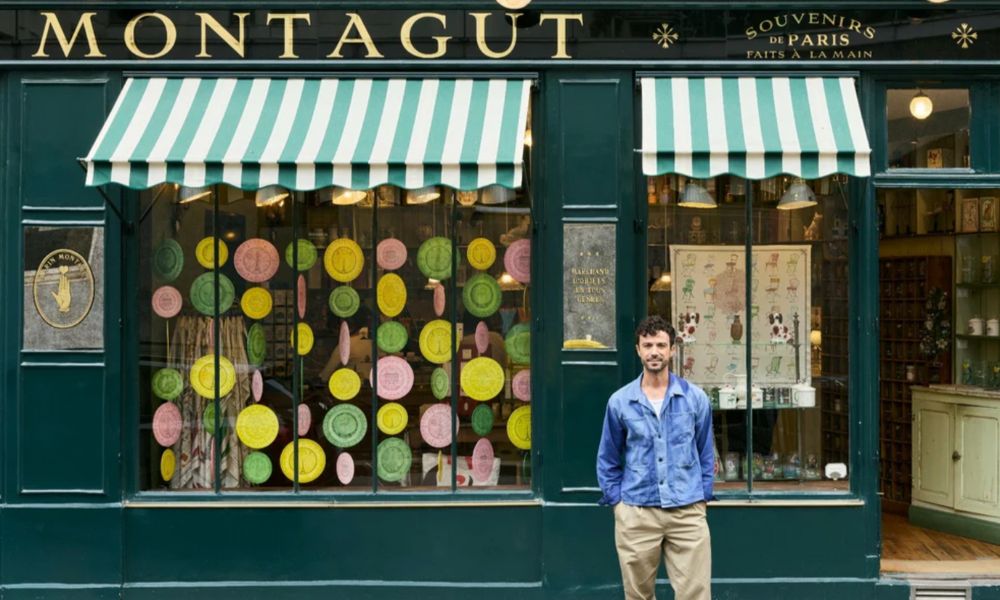 This is an image of a man standing in front of a gift store with a bunch of cool things in the window.