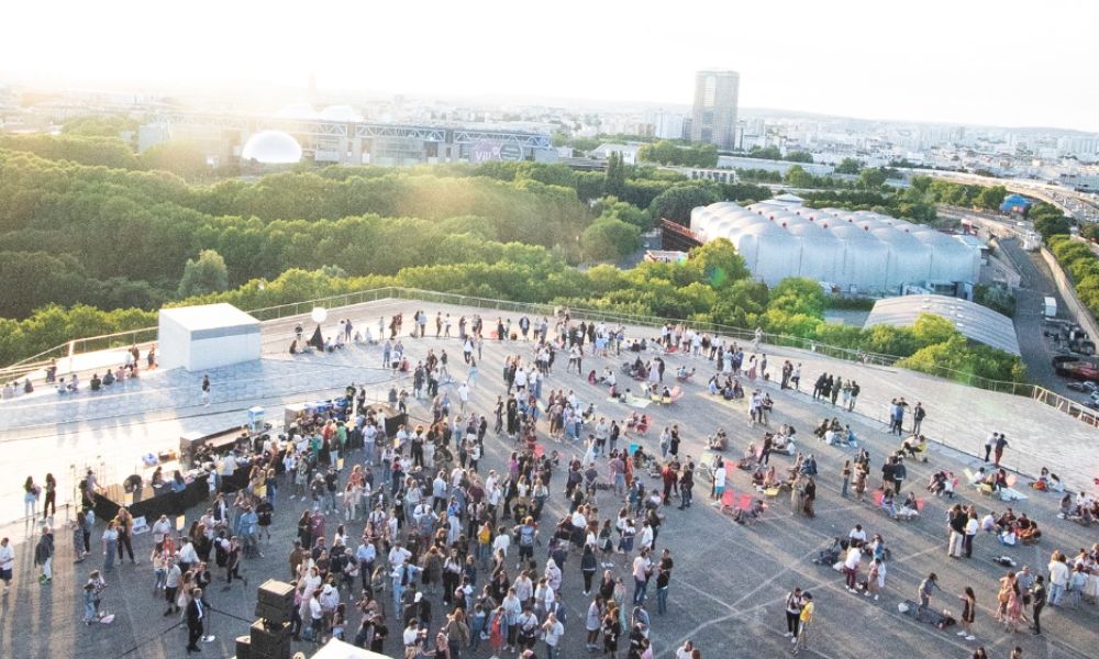 This is an image of a lot of people on the terrace of a building looking out on to the city afar.
