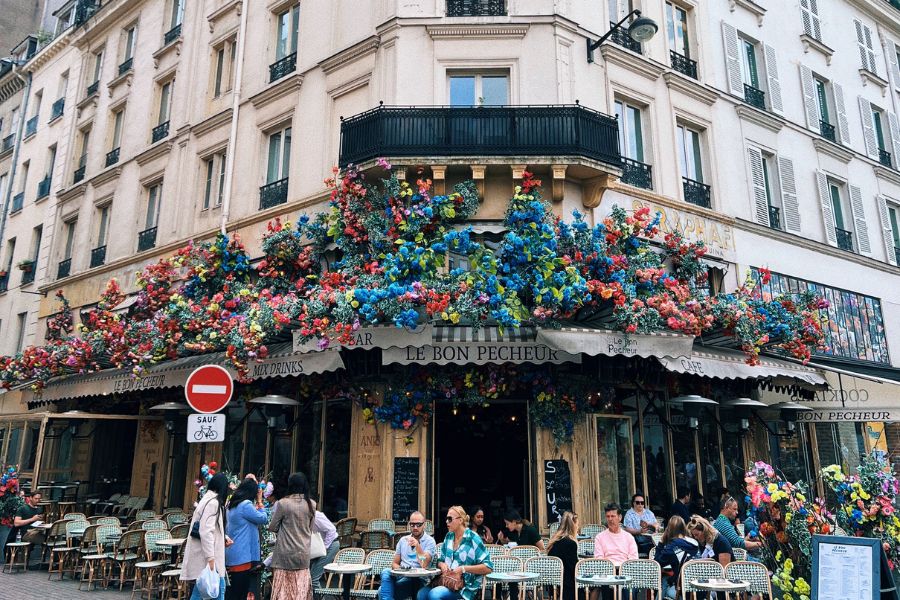This is an image of a cafe with people sitting on tables outside.