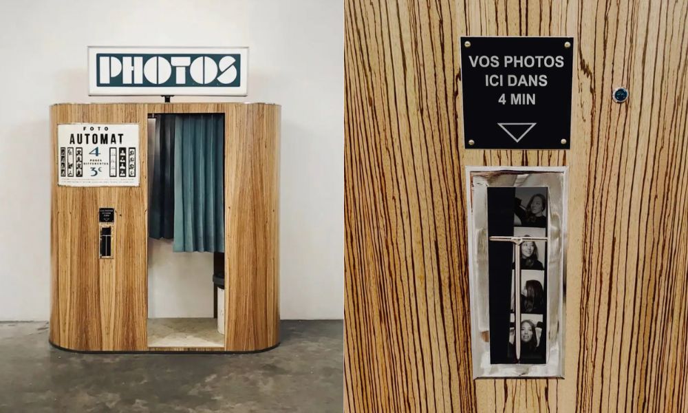 This is an image of a wooden photobooth with a blue curtain and someone's strip photos in the collection point.
