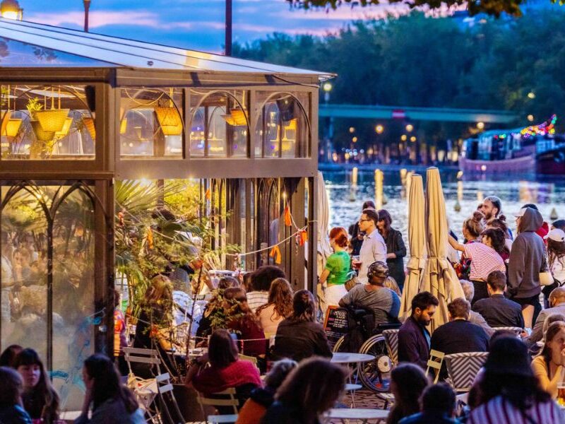 This is an image of a big outdoor deck space with people sitting on tables talking.