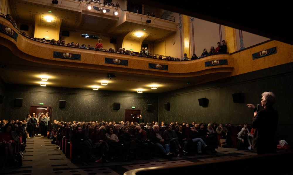 This is an image of an old theatre cinema with plenty of people looking on to someone speaking at the front.