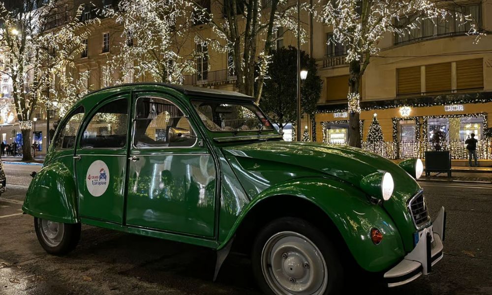 This is an image of a small tour car parked up in front of a big building with Christmas lights in front of it.