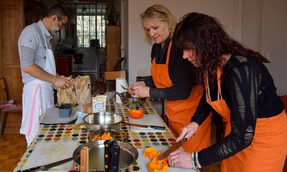 This is an image of people cutting up vegetables on a table and cooking together.