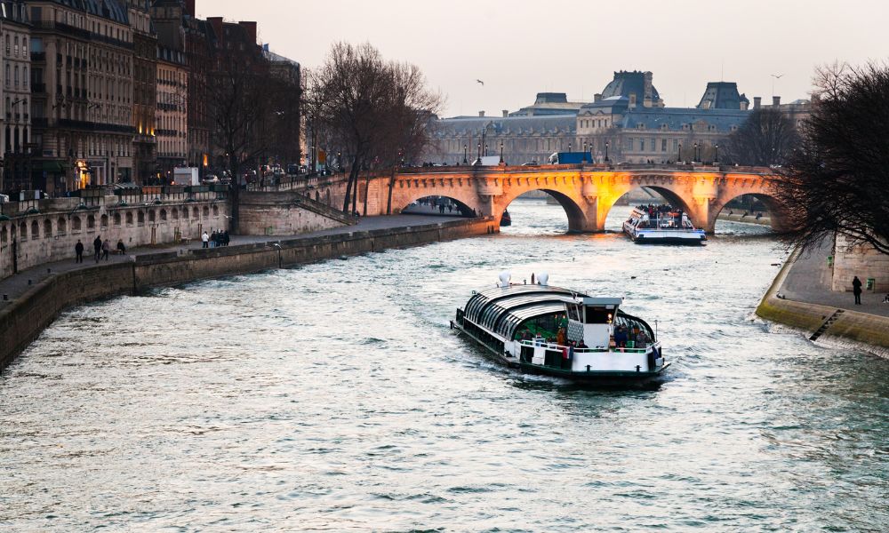 This is an image of a boat churning through the Seine at dusk with an arched bridge coming up in the distance.