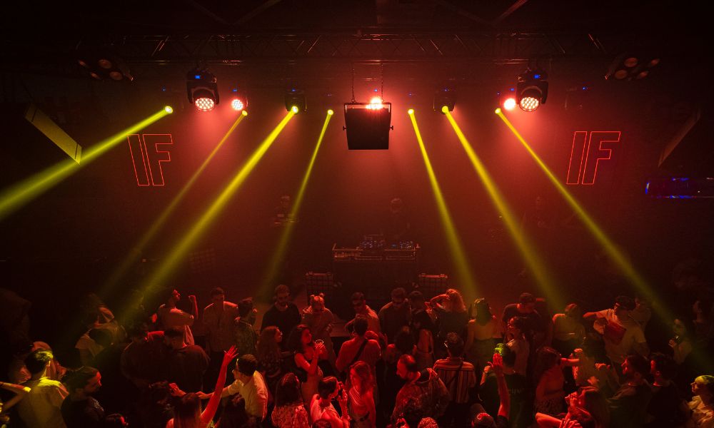 This is an image of lots of people in a nightclub dancing with big lights shining on them.