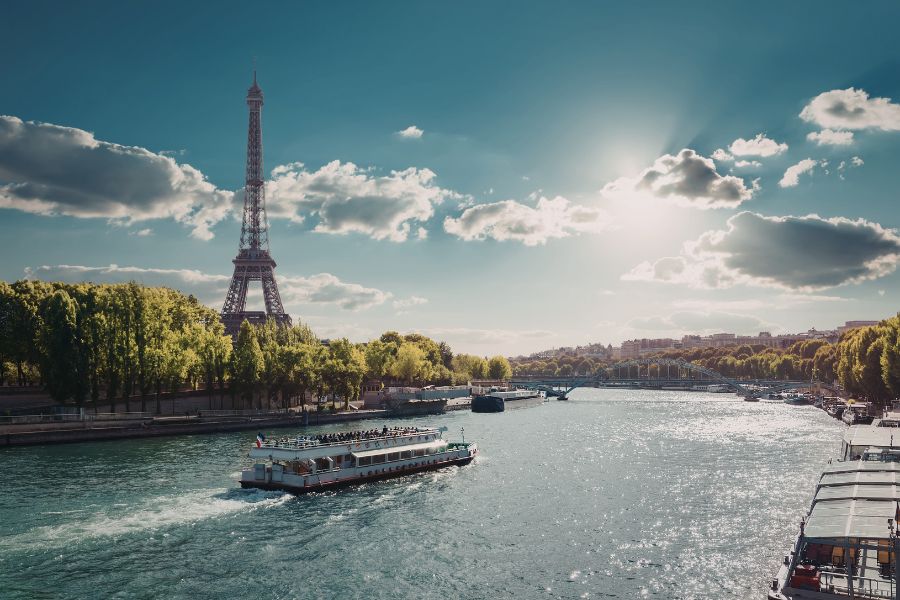 This is an image of a boat in the middle of the Seine river with the Eiffel Tower behind it in the distance.