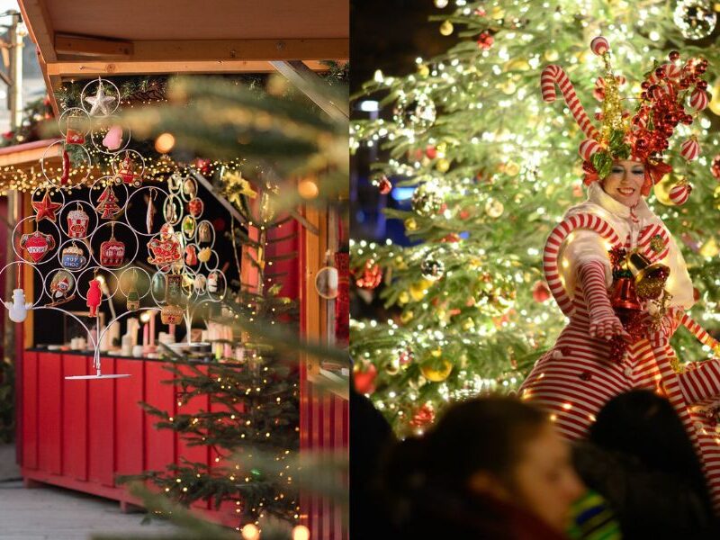 This is an image of a Christmas stall with with loads of ornaments for sale. To the right is a lady on stilts in front of a Christmas tree.