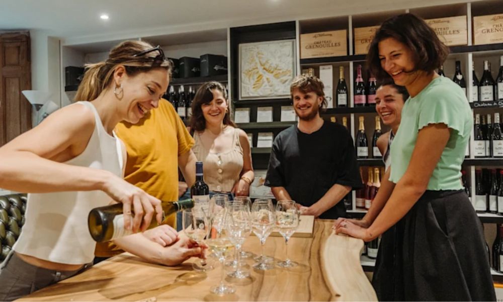This is an image of a group of people standing around a table laughing with a tour guide pouring wine.
