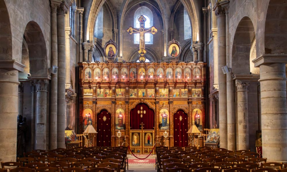 This is an image of a church with lots of pews, stained-glass windows and a big cross overhead.