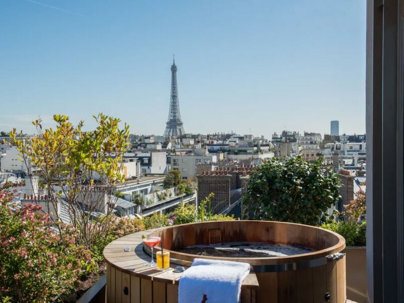 This is an image of a spa with towels draping around the sides and cocktails ready to drink. The spa overlooks a view of Paris including the Eiffel Tower.