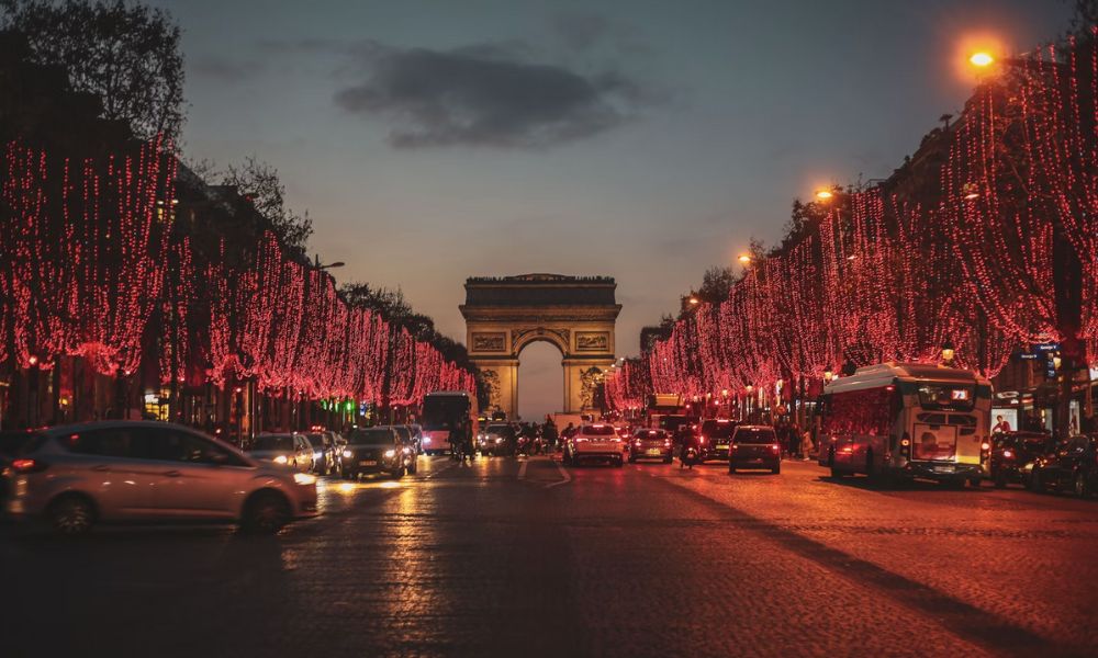 This is an image of the Arc de Triomphe with trees lining the street leading up to it, which are all dressed with red Christmas lights.