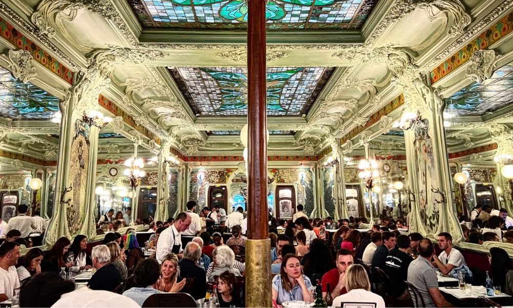 This is an image of a beautiful restaurant with beautiful detailing on the walls and roof with lots of people inside.