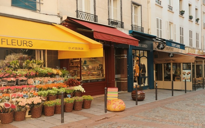 A quite street in Paris, with a flower shop with baskets of flowers outside