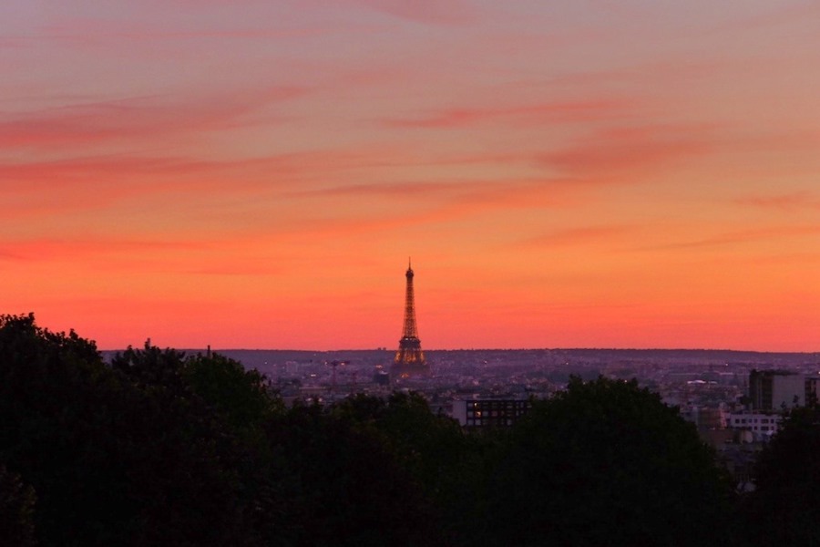 This is an image of Paris's sprawling city taken from the top of a hill with a prominent centre view of the Eiffel Tower and a burnt orange sunset around it.