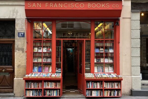 This is an image of a big, red building with books lining the front area/ There are also big glass windows showing the inside that contains plenty more books.