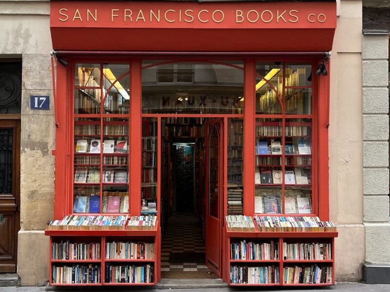 This is an image of a big, red building with books lining the front area/ There are also big glass windows showing the inside that contains plenty more books.