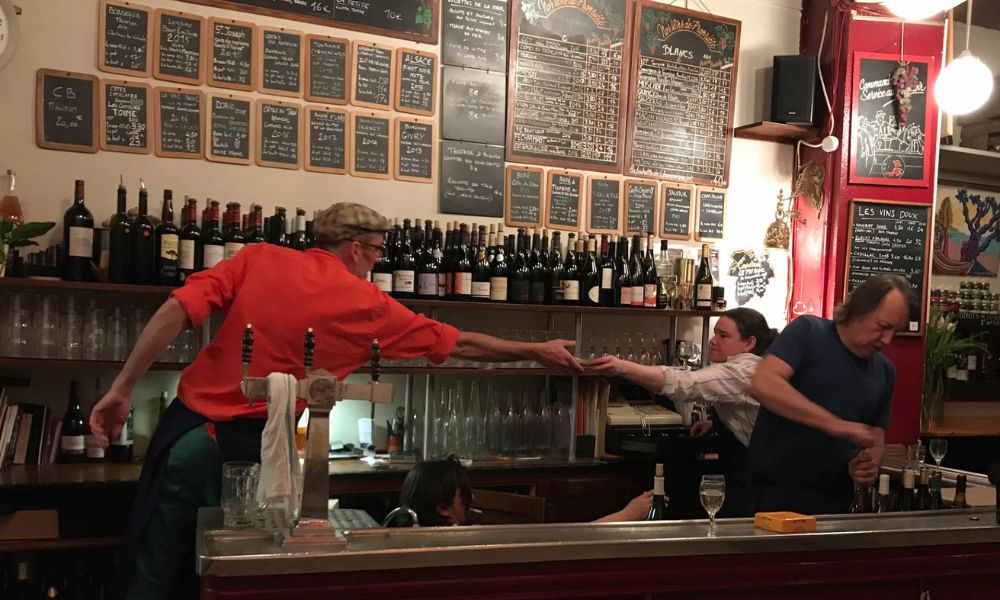 This is an image of a wine bar with lots of bottles of wine and workers behind the bar.