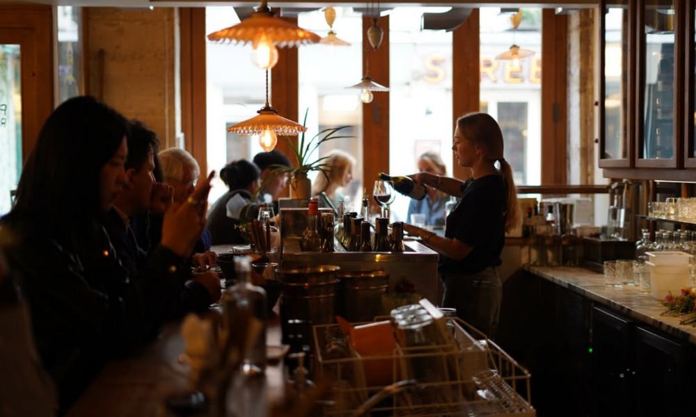 This is an image of a group of people sitting on the wine bar with a person behind the bar making drinks.