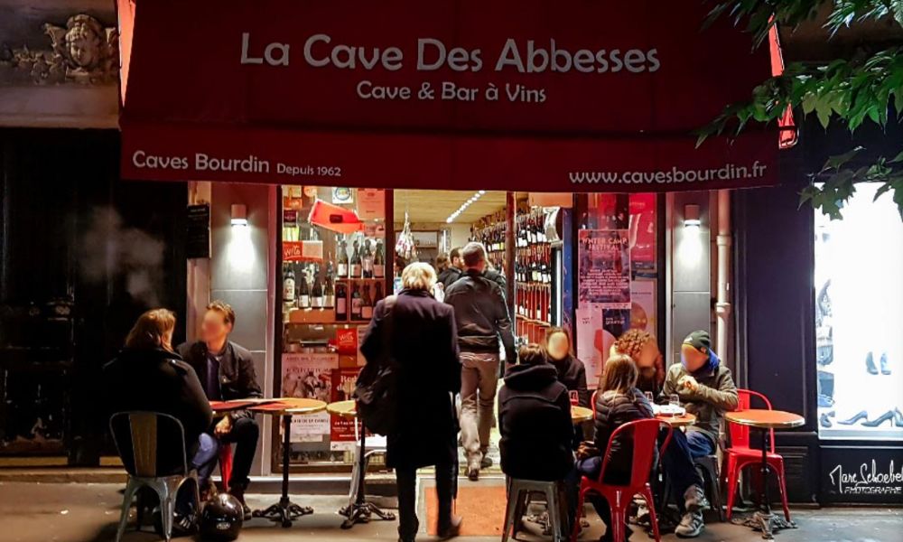 This is an image of a wine bar in the city with a red veranda and people milling outside.