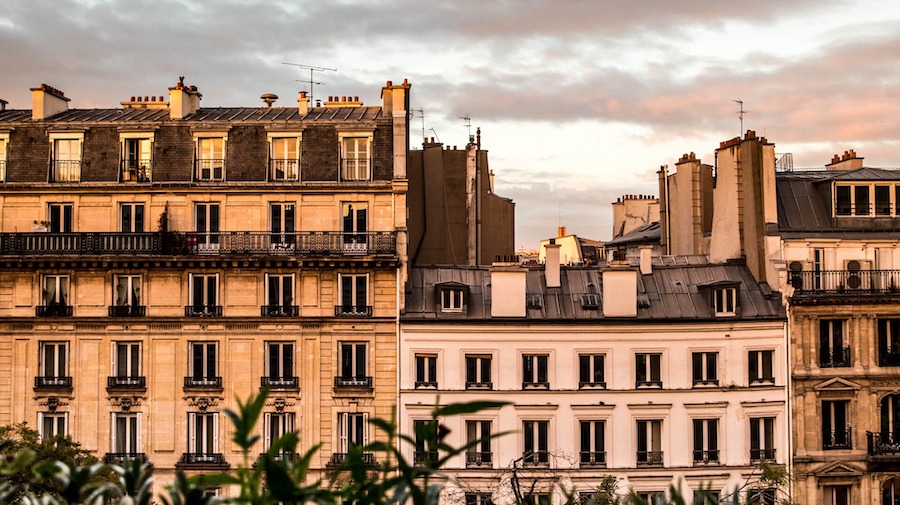 This is an image of the view of a beautiful hotel front in Paris with the sun setting in the background.