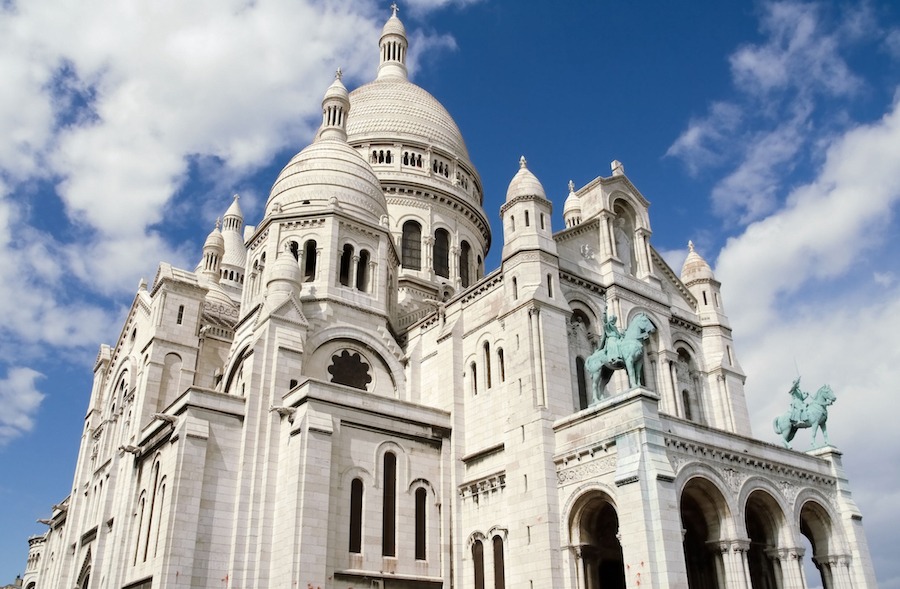 This is an image of the front of a famous landmark in Montmatre with greyish white stone walls and sculptural features.