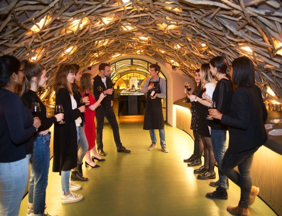 This is an image of a wine tour with people drinking and serving different types of wine in a cellar.