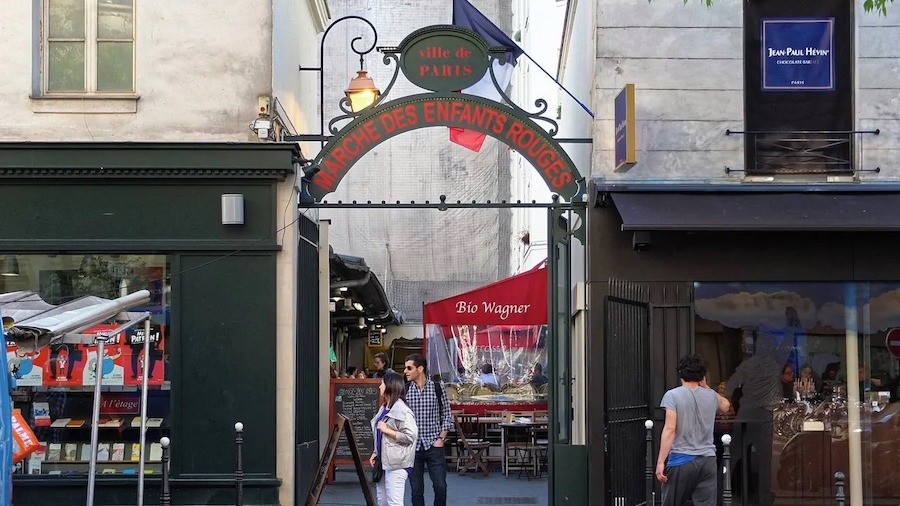 This is an image of the outside entrance to a French market with a few people stood outside walking around the area.