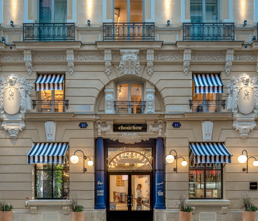 This is an image of the front of a whimsical looking hotel in Paris with beige walls and blue and white striped features.
