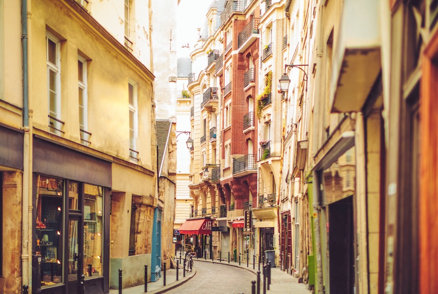 This is an image of the Latin Quarter area in Paris which is a cool bohemian area full of shops. The image shows a winding street with eclectic looking storefronts and bars.