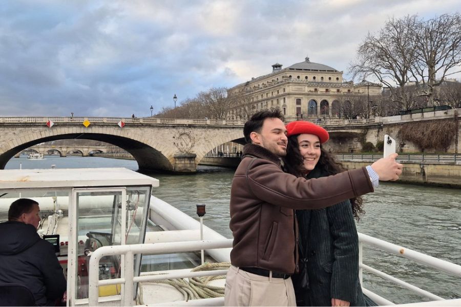 This is an image of a couple posing for a photo while taking a boat on the Seine and standing in front of a bridge.