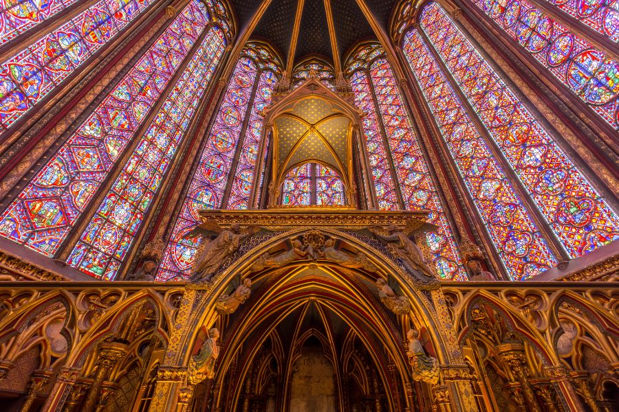 This is an image of a pretty church with purple-stained glass windows and gold detailing around the room.