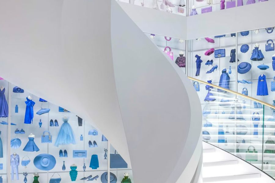 This is an image of a museum with stairs and a bunch of cool dresses and bags propped up in the window.