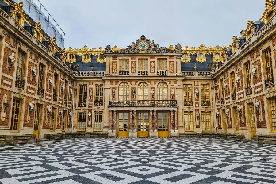 This is an image of a big majestic castle-like building with big windows and checked tiles out the front.