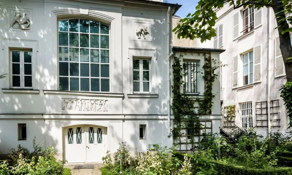 This is an image of a big, manor-esque white building with greenery surrounding.