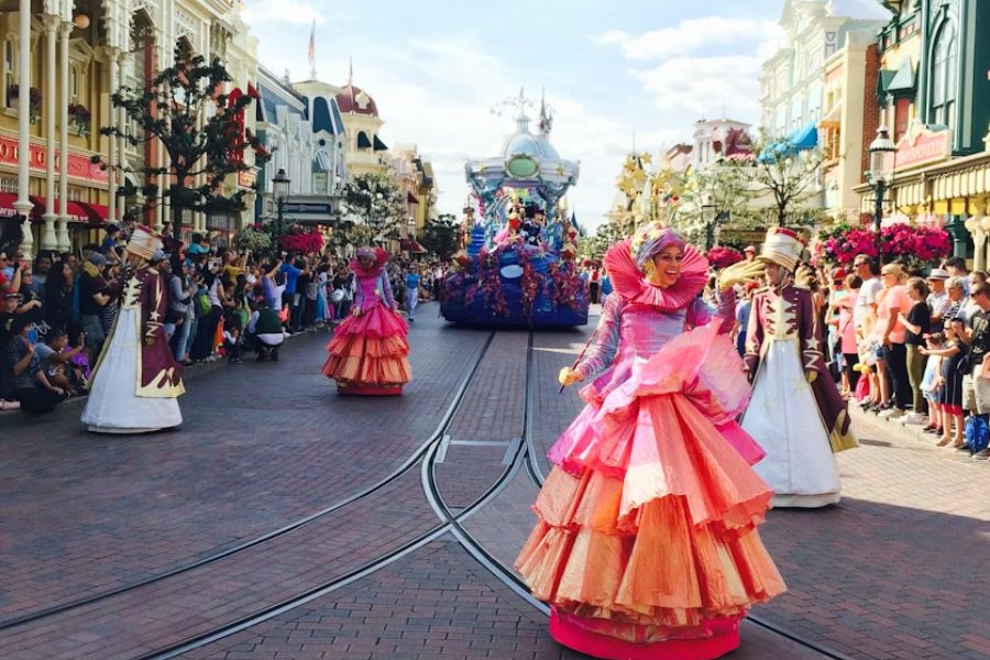 This is an image of a bunch of people dressed in big fluffy dresses while a Disneyland float charges up ahead of them.