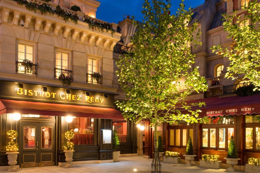 This is an image of a restaurant with lights on inside and trees lining the front