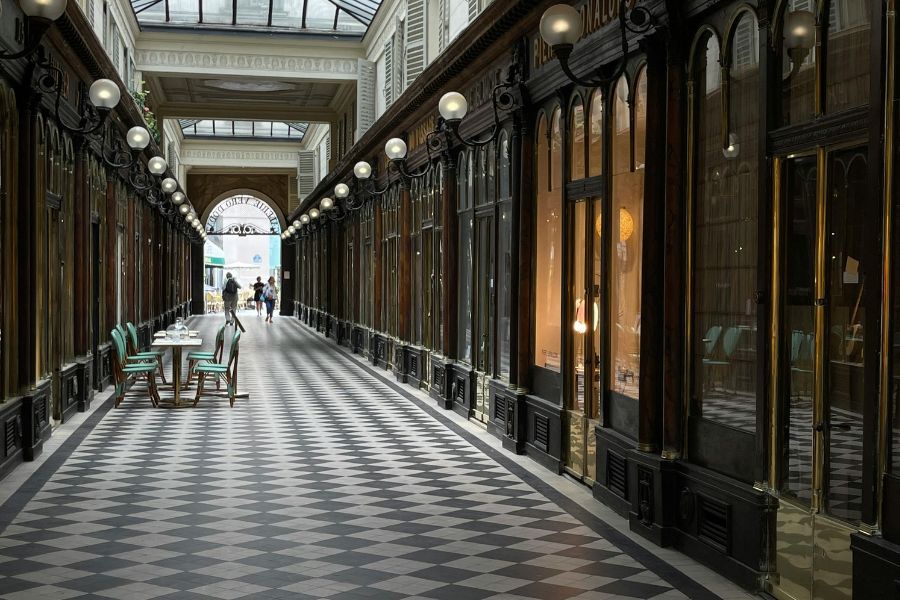 This is an image of a long passageway with checkered flooring and shop fronts lining the whole way down.