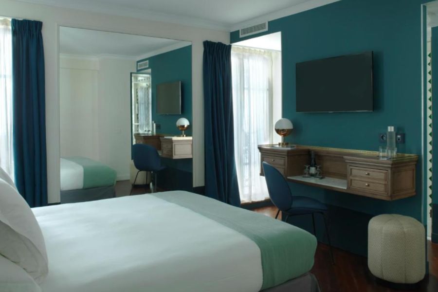 This is an image of a dark room with blue walls and a double bed, with a massive mirror and desk.