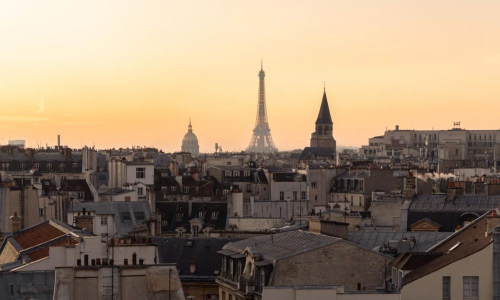 This is an image of Paris from above with a view of the Eiffel Tower in the distance. The backdrop is a hazy orange and yellow sky.