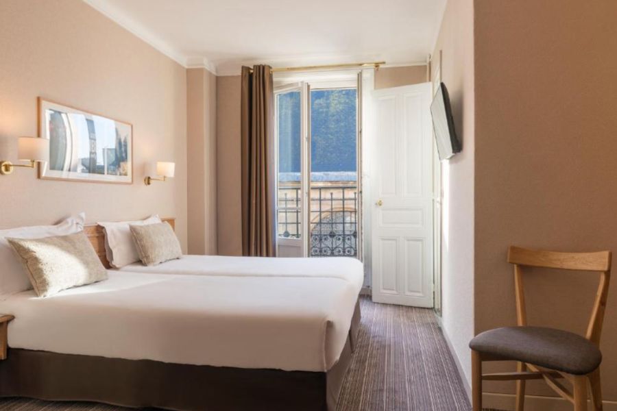 This is an image of a minimalist hotel room with white sheets, and twin single beds, plus a door to an outdoor balcony.