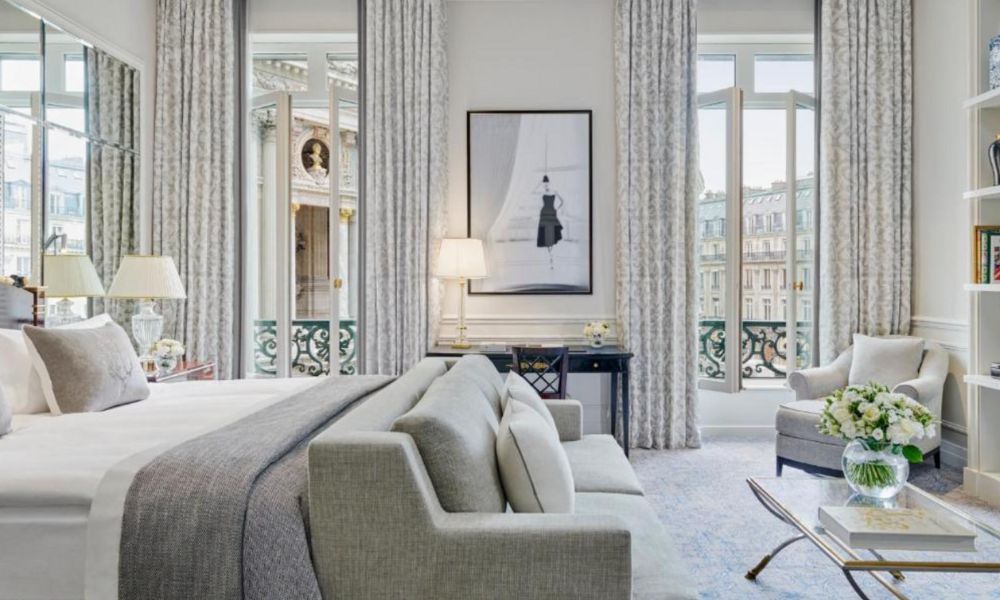 This is an image of a white minimalist hotel room with a bed, couch and big lounge area. There are also amazing floor to ceiling windows.