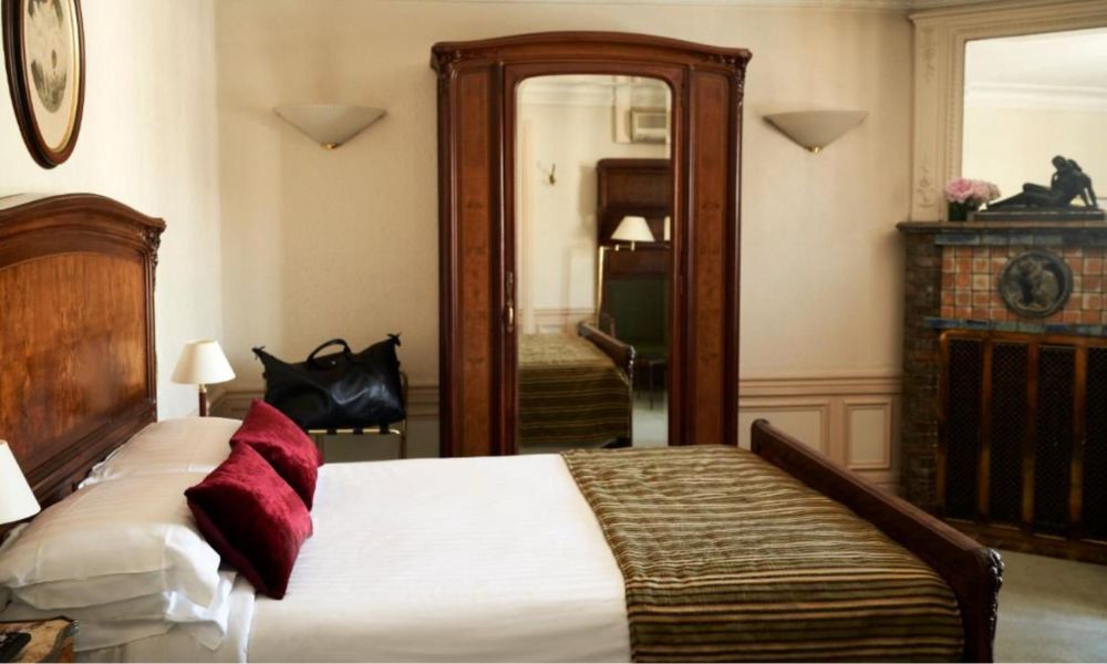 This is an image of a clean, simple hotel room with wooden furniture and plain white bedding.