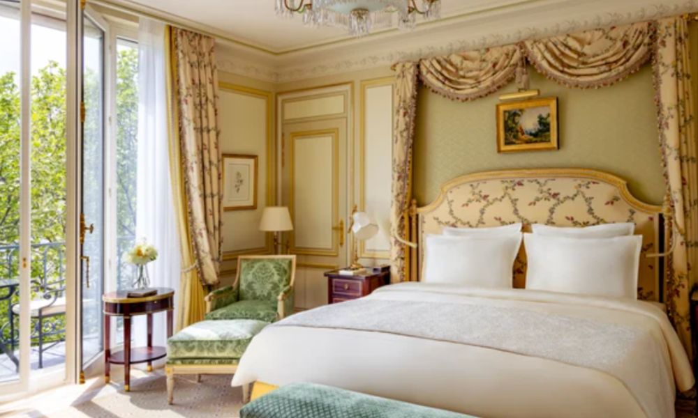 This is an image of a regal hotel room with a bed and curtain draping. There is also a really nice window and balcony.