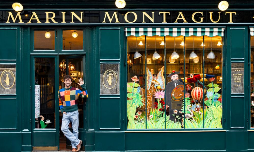 This is an image of a souvenir shop with a man standing in the doorway smiling, next to a big window with graphics and detailing painted on the front.