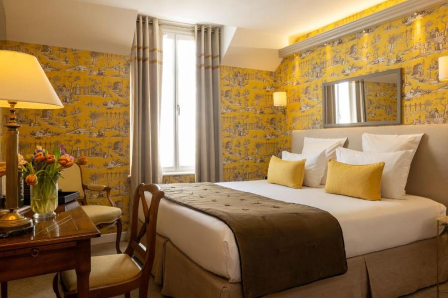This is an image of a hotel room with a double bed, a desk and yellow feature walls.